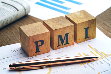 Text "PMI" on wood cube and gold pen lay on chart candle document paper , economic data concept.
