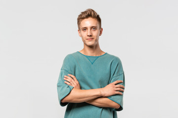 Confedent young man in a green tee holds hands folded isolated over grey background.