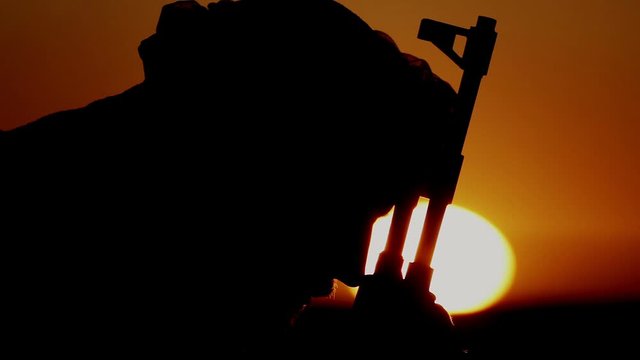 Portrait of a Muslim warrior bowing his head over a machine gun. Islamic militant prays to Allah over the machine gun.
