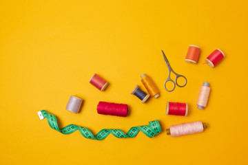 Multi colored threads pink reels, measuring tape, sewing machine needles on a background. Sewing accessories for needlework, sewing. Place for text.