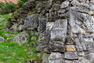 A bunch of pageant fragments of the fortress, stones with Hellenistic patterns. Green grass on a hill, excavation of structures, beautiful natural background backdrop texture