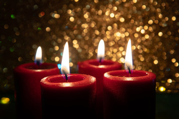 Advent theme with 4 burning red candles. Christmas decoration. Sparkling gold background. Darkness, selective focus.