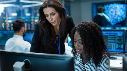 Female Team Leader Consults Young Computer Engineer. They Work in a Crowded Office on a Neural...