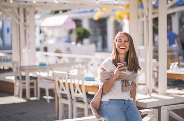 Beautiful smiling woman holding paper coffee cup to go and enjoying the walk in the city in autumn.