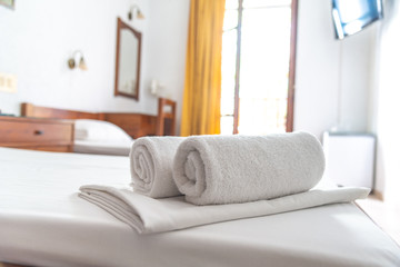 Two white towels are on the bed in hotel room. Close-up horizontal background. Space for text.