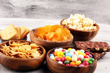 Salty snacks. Pretzels, chips, crackers in wooden bowls and candy and chocolate on table