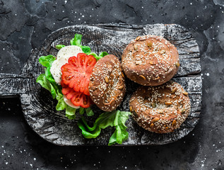 Multigrain multiseed fitness buns and green salad tomato homemade cheese sandwich on dark background, top view. Healthy diet food concept