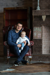 A father sits in a chair and holds his little son in his lap. They are both smiling. Family life.