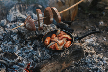 Roasted potatoes in rind with bacon, meat. Fried potatoes in a frying pan in the woods. Bread fried on a fire. Camping with food. Picnic on a stump with tea. Fried sausages. To eat in nature