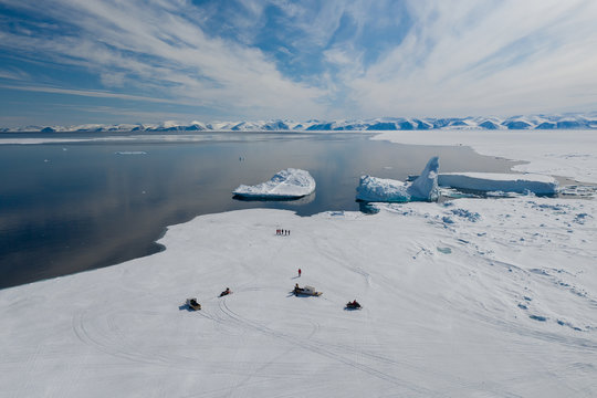 Aerial drone photo of tourists travelling by Qamutiik on the sea ice near Sirmilik National Park in Nunavut, Canada