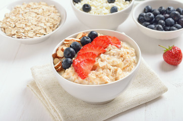 Fototapeta na wymiar Oatmeal porridge with strawberry slices, blueberries and nuts