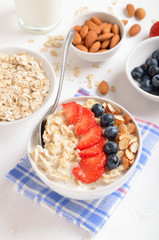 Oatmeal porridge with strawberry slices, blueberries and nuts in bowl
