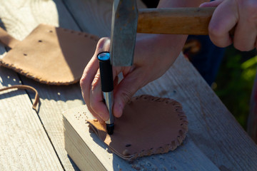 close-up of women's hands making holes to make a wallet of genuine leather