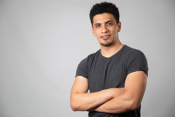 Young Hispanic man with arms crossed smiling, brunette man in studio looking at camera