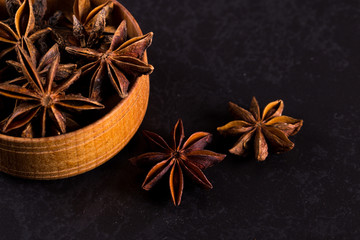 Star anise in a wooden bowl on a black table. Concept, copy space.