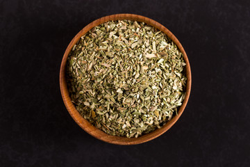 Crushed oregano scattered in a wooden bowl on a black table. Concept, copy space.