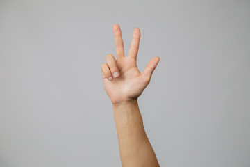 Man's hand with number three, hand raising three fingers up in studio with gray background