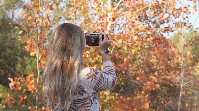 Girl in the autumn forest with an old camera takes pictures of nature