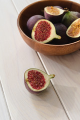 Obraz na płótnie Canvas Ripe fresh fig fruits lie in a wooden bowl on a light wood background. Healthy fruit snack. Whole figs and slices. View from above.