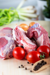 Raw meat slices on chopping board with fresh vegetables and spices