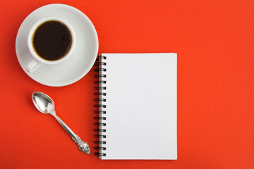 Obraz na płótnie Canvas Open notepad and black coffee in the white cup on the red background. Copy space. Top view.
