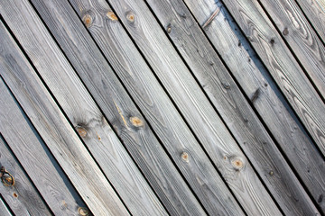 The wall of old boards natural wood. Weathered planks with a diagonal pattern. The tree darkened under the sun. The clear structure of the tree under the sun.
