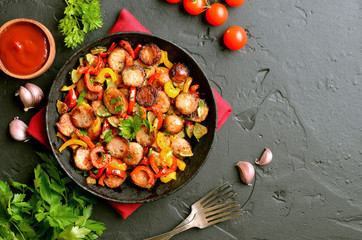 Slices of fried vegetables with sausages and spices in frying pan
