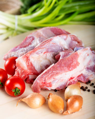 Raw meat slices on chopping board with fresh vegetables and spices