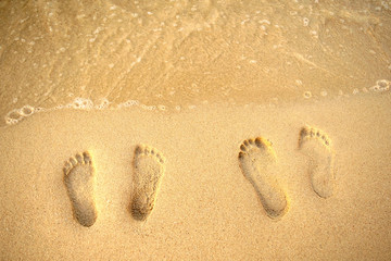 Feet prints on the sand of the beach and sea wave. Top view. Two people foot marks on sand. 