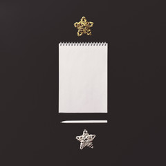 A notebook with blank sheets is on a black background. Nearby are white and yellow wicker stars and a white handle. Image on the subject of planning, records, goal setting.