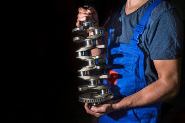 Auto mechanic with a crankshaft in his hands, on a black background. Auto engine repair services.