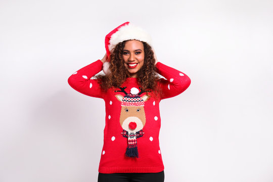 Studio portrait of young woman with dark skin and long curly hair wearing tight santa claus hat and christmas outfit. Ugly sweater concept. Close up, copy space for text, isolated background.