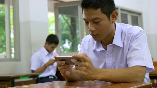 Asian high school students in a white uniform, who are a lot of addicted to games. They are playing exciting games on  their mobile phones and sitting in the classroom.
