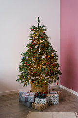 room Christmas tree decorated with red, white and emerald balls, gifts under the tree lie, Christmas room decor with white and pink walls