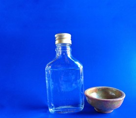Bottle of brandy with clay cup on blue background. typical alcoholic drink of Guatemala