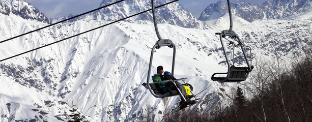 Fototapeta na wymiar Skiers on ski-lift and snow mountains at winter sun day