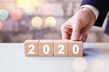 Businessman hand arranging wood block with new year 2020 on bokeh background.