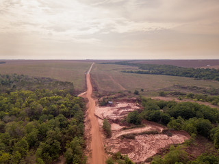 Drone aerial view of dirt road in forest with huge soybean plantation area in the background near Sinop city, Mato Grosso, Brazil. Agriculture, conservation and deforestation concept.