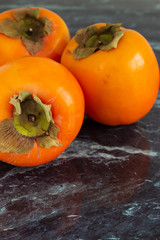 Top view of three orange kakis on dark marble in vertical with copy space