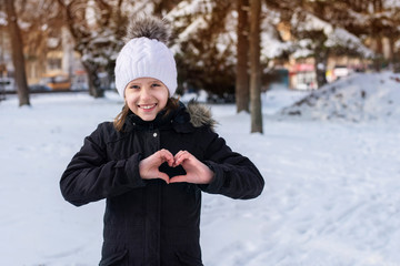 Teenage girl walking through the city in winter and enjoys a snowy city, nature, girl smiles and shows heart by her hands because she loves winter