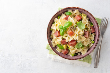 Farfalle pasta salad with smoked tuna, avocado, capers and greens in bowl on concrete background. Top View. Copy space.