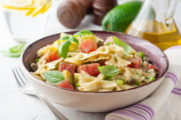 Farfalle pasta salad with smoked tuna, avocado, capers and greens in bowl on concrete background. Selective focus.