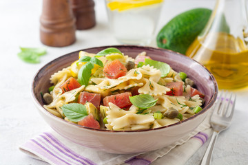 Farfalle pasta salad with smoked tuna, avocado, capers and greens in bowl on concrete background. Selective focus.