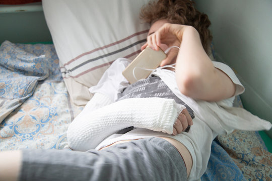 A patient with a broken arm is lying in hospital on a bed.