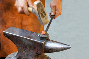 Blacksmith manually forging the molten metal on the anvil in smithy.