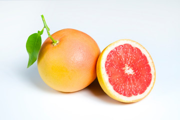 Close up image of juicy organic whole and halved grapefruits with green leaves & visible core texture, isolated background, copy space. Macro shot of bright citrus fruit slices. Top view, flat lay.