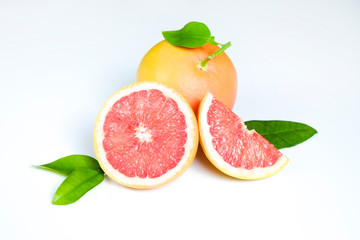 Close up image of juicy organic whole and halved grapefruits with green leaves & visible core texture, isolated background, copy space. Macro shot of bright citrus fruit slices. Top view, flat lay.