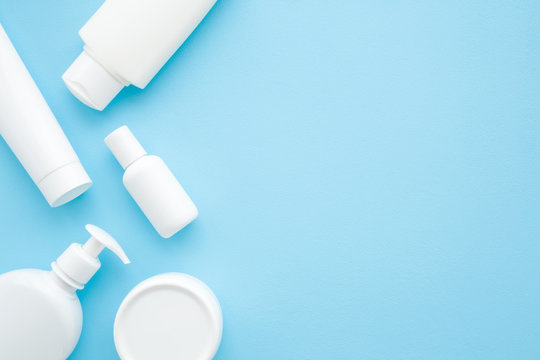 Different white toiletries on light pastel blue table. Care about face, hands, legs and body skin. Women beauty products. Empty place for text or logo. Flat lay. Top down view.