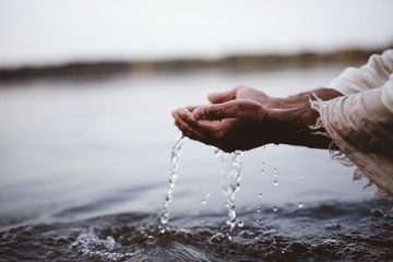 Closeup shot of a person wearing a biblical robe drinking water with hands