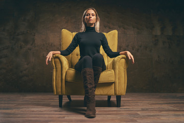 Beautiful young stylish woman in black wear sitting in yellow armchair.